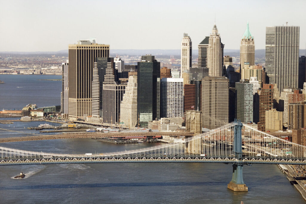 Aerial view of New York City's Manhattan Bridge with Brooklyn Bridge and Manhattan buildings in background.