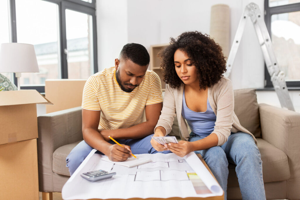 African American couple with blueprint and calculator counting money for repair costs to new home