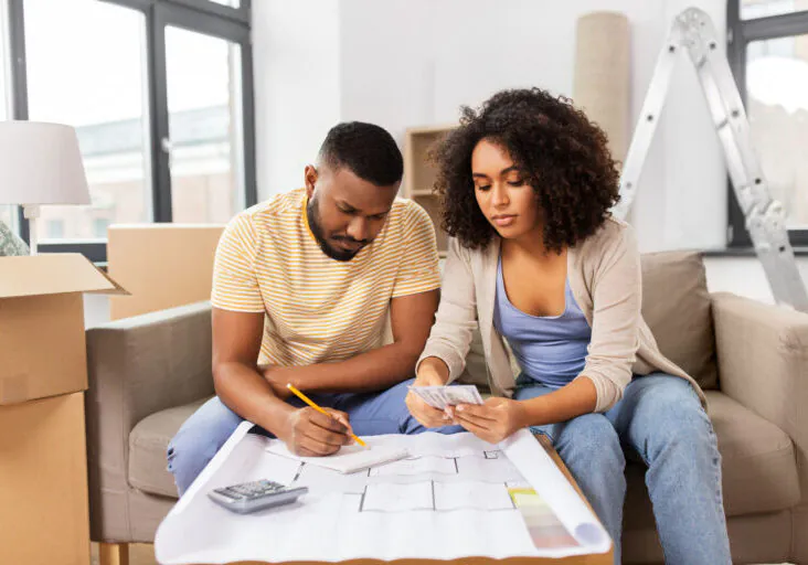 A couple surrounded by moving boxes comparing costs with a calculator