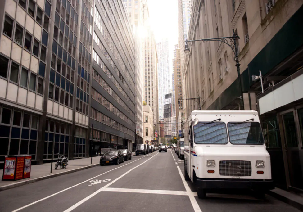 A box truck parked at the curb on a narrow Manhattan street lined with tall buildings